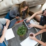 a group of women sitting around a table working on a laptop