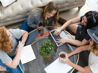 a group of women sitting around a table working on a laptop