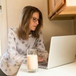 A woman working on a laptop in a home kitchen, illustrating remote work lifestyle.