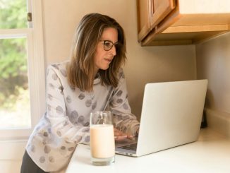 A woman working on a laptop in a home kitchen, illustrating remote work lifestyle.